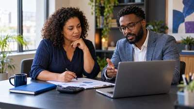 Dona de PME brasileira e consultor analisam orçamento de marketing, calculadora, notebook e pasta azul; conversa ponderada sobre investimento.